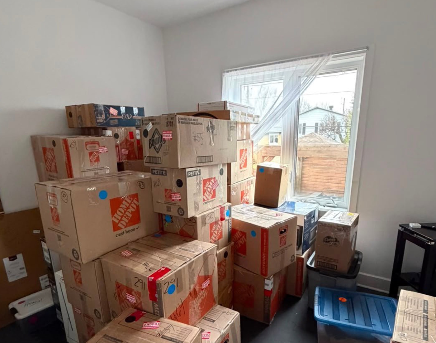 Gros plan de boîtes empilées près d’une fenêtre, certaines marquées à la main.