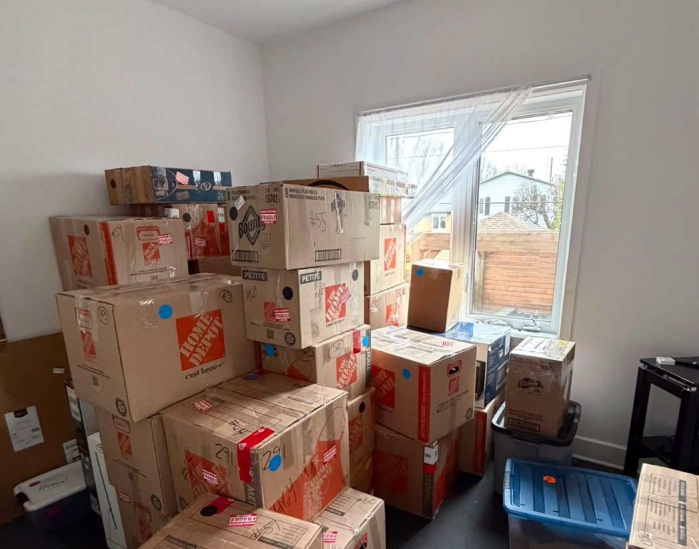 Close view of stacked boxes by a window, some marked by hand.
