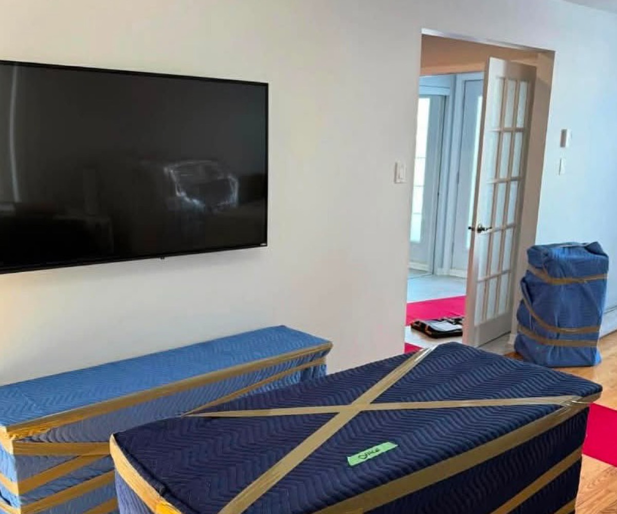 A covered piano in front of a television, with a door open to another room.